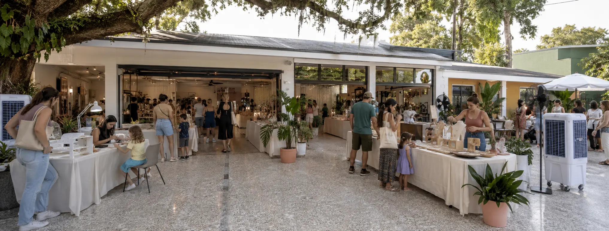 A modest community maker event extends from an open Florida storefront onto a live-oak-shaded terrazzo courtyard.