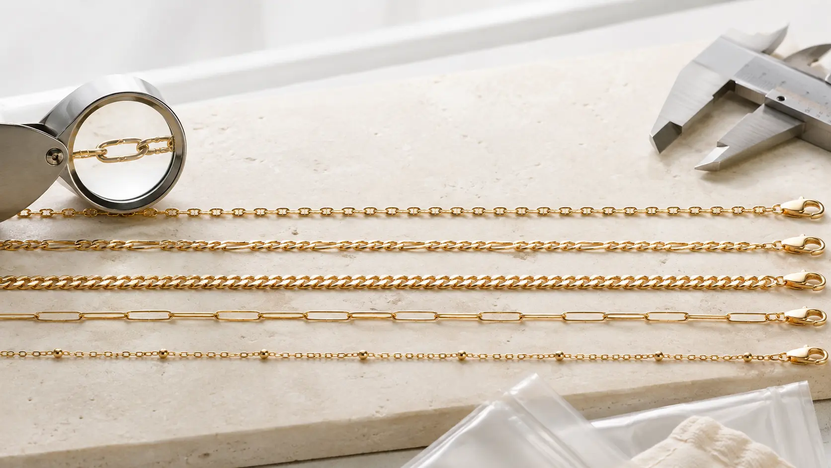 Five gold chain structures are aligned at true relative scale with a loupe and caliper.